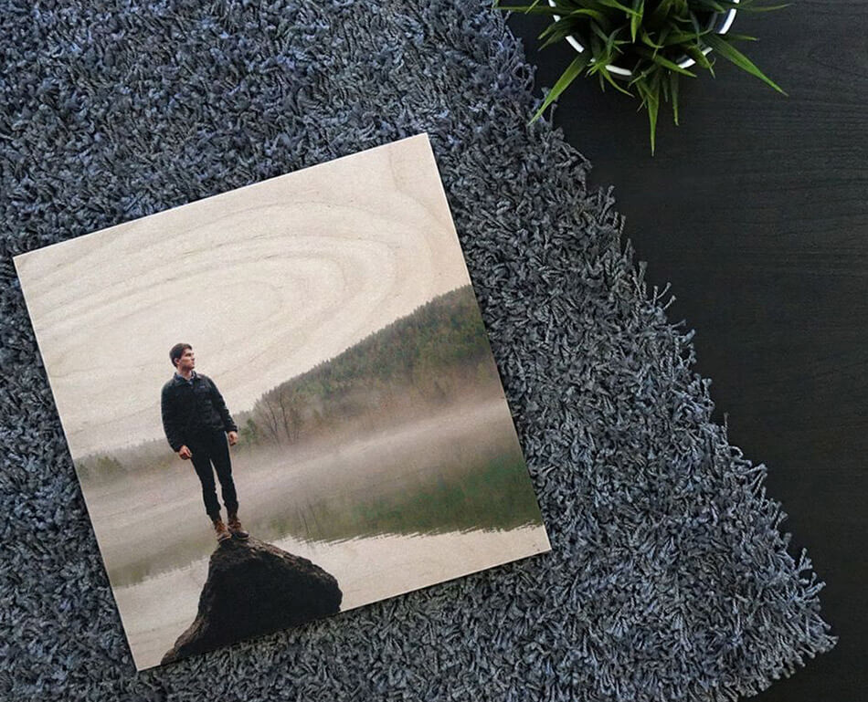 A photoboard wood print of a man and a lake, laying on a grey shag rug