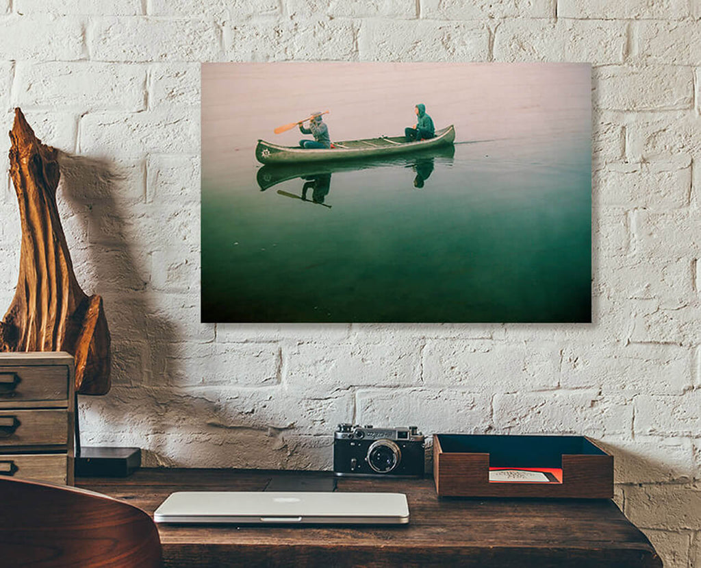 A readymade wood print on a white brick wall. Two young men in a canoe on a semi-transparent lake.