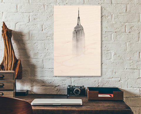 A readymade wood print on a white brick wall. The top of the Empire State Building fading into wood grain.