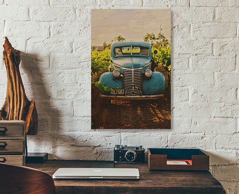 A readymade wood print on a white brick wall. An old, blue Chevrolet truck sitting in a field.